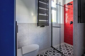 A bathroom with a white toilet, a glass shower enclosure, and a red-tiled shower area.