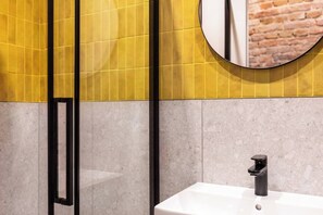 A bathroom with a yellow tiled wall, a round mirror, a black faucet, and a white sink. - The Geometric 3-bedroom apartment (Kraków – Old Town)