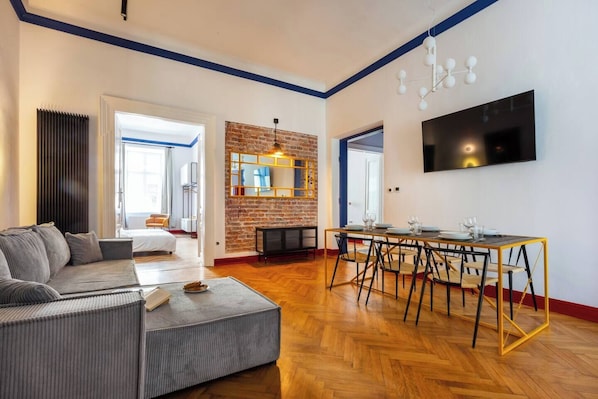 A modern living room with a sofa, dining table, and a TV mounted on the wall.