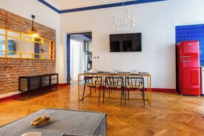 Un salon moderne avec un mur en briques, une table à manger dressée pour quatre personnes, un réfrigérateur rouge et un téléviseur fixé au mur.