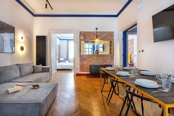 A modern living room with a sofa, dining table set for four, and a brick accent wall. - The Geometric 3-bedroom apartment (Kraków – Old Town)
