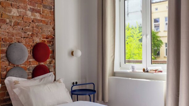 Une chambre avec un mur en briques, un lit, une fenêtre donnant sur un paysage verdoyant et une chaise bleue.