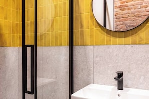 A bathroom with a yellow tiled wall, a round mirror, a black faucet, and a white sink.