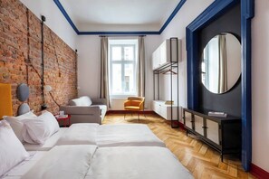 Une chambre d’hôtel avec un mur en briques, une grande fenêtre, un lit, une chaise, un bureau et un miroir.