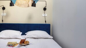 Una habitación de hotel con cama, almohadas, una lámpara de pared, un cuadro y un plato con comida.