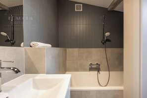 A modern bathroom with a bathtub, two showerheads, and a towel rack.