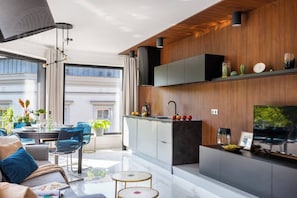 A modern kitchen with a built-in oven, a dining area with a table and chairs, and a large window providing a view of the city. - Apartment Modern Spacious (Kraków – Modern View of Planty Park)