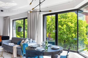 Ein modernes Wohnzimmer mit Sofa, Esstisch und großen Fenstern mit Blick ins Grüne.