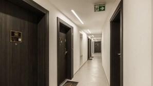 Ein Hotelkorridor mit dunklen Holztüren, einem grünen Notausgangsschild und einem QR-Code an der Wand.