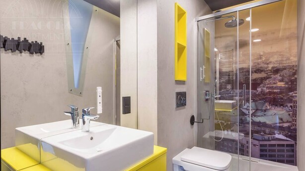 A modern bathroom with a white sink, yellow vanity, and a glass shower enclosure with a cityscape view. - Apartment Modern Industrial (Kraków – Modern View of Planty Park)