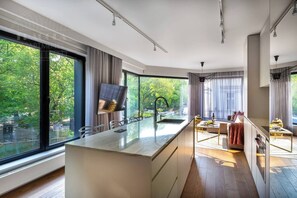 A modern kitchen with a large island, a dining area, and a view of greenery outside. - Apartment Modern Marble (Kraków – Modern View of Planty Park)