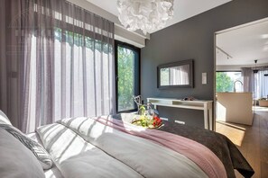 A modern bedroom with a large bed, a desk, and a view of the outdoors.