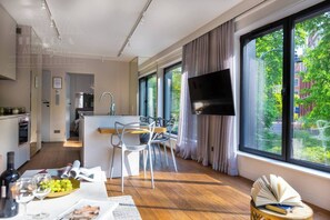 A modern kitchen with a dining area, large windows, and a flat-screen TV. - Apartment Modern Marble (Kraków – Modern View of Planty Park)