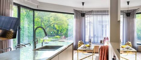 A modern kitchen with a large window, a flat-screen TV, and a dining area with a table and chairs.