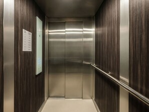 An elevator with a metallic interior, a wall-mounted directory, and a handrail. - Apartment Modern Marble (Kraków – Modern View of Planty Park)