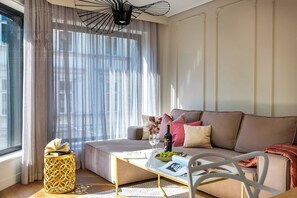 Een moderne woonkamer met een bank, een salontafel, een bijzettafeltje met boeken en een raam met dunne gordijnen.