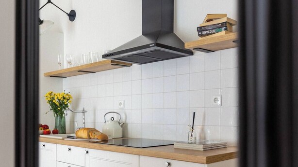 A modern kitchen with white cabinets, a wooden countertop, a stainless steel range hood, and a vase of yellow flowers. - Canvas House Apartament Oatmeal (Kraków)