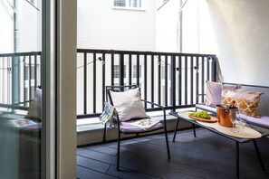 A balcony with a chair, a table with a bucket of grapes and a bottle, and a sofa with cushions. - Canvas House Apartament Oatmeal (Kraków)