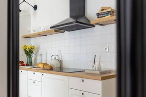 A modern kitchen with white cabinets, a wooden countertop, a stainless steel range hood, and a vase of yellow flowers. - Canvas House Apartament Oatmeal (Kraków)