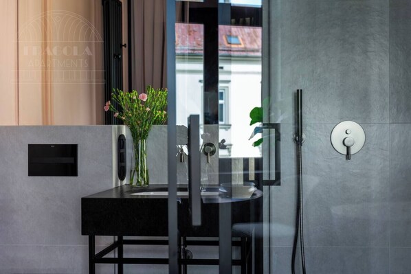 A modern bathroom with a glass shower enclosure, a sink with a vase of flowers, and a visible window.