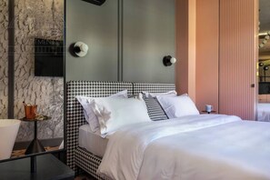 Una habitación de hotel moderna con un cabecero estampado en pata de gallo, una cama grande con sábanas blancas, una mesita de noche pequeña con una lámpara y un espejo en la pared.