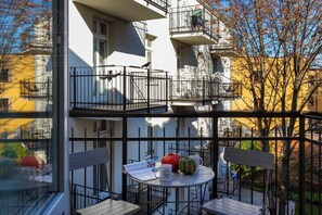 A multi-story building with balconies, a round table with chairs, and a window with a view of the surrounding area.