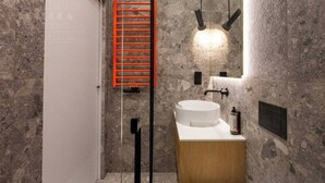 A bathroom with a stone wall, a white sink, a wooden cabinet, a red ladder, and a mirror with lights.