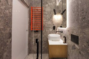 A bathroom with a stone wall, a white sink, a wooden cabinet, a red ladder, and a mirror with lights.