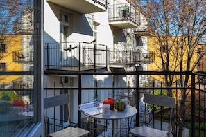 Un edificio de varios pisos con balcones, una mesa redonda con sillas y una ventana con vista al entorno.
