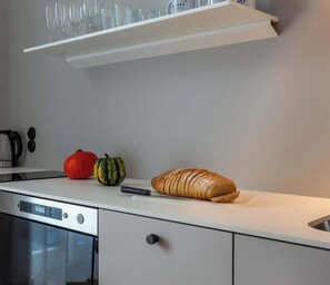 A modern kitchen with a white countertop, a loaf of bread, a red bell pepper, and a small squash.
