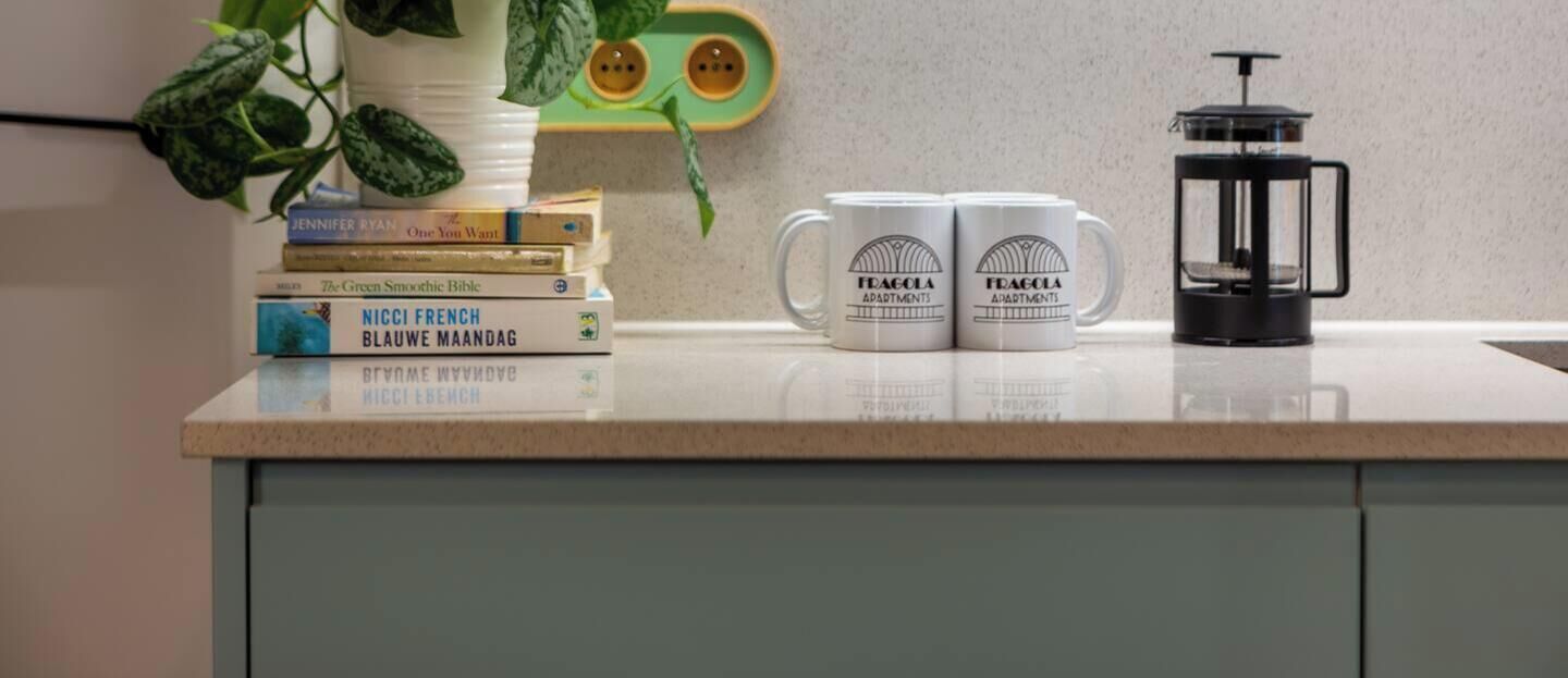 A kitchen counter with a coffee maker, two mugs, and a stack of books.