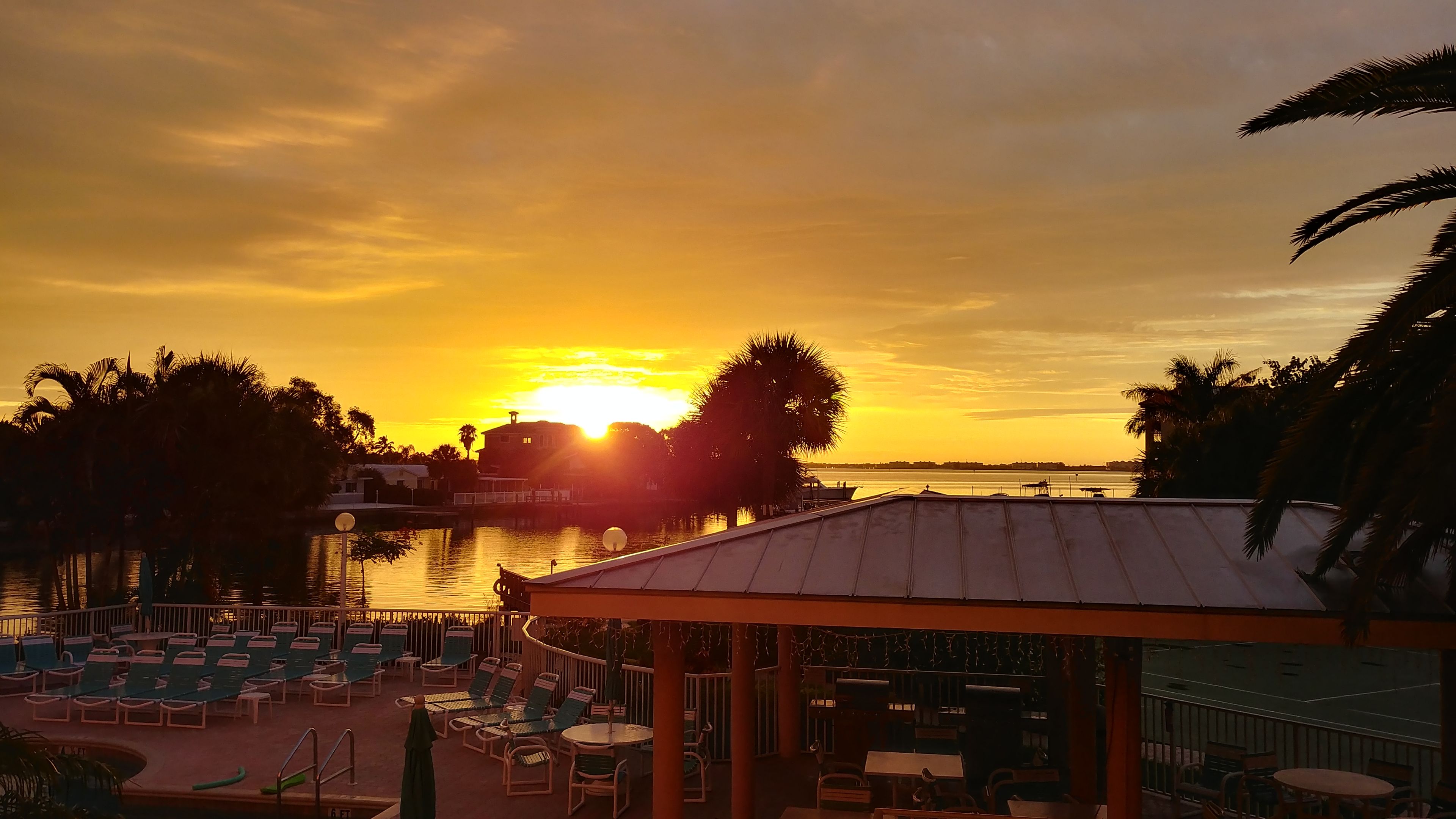 Une vue sur le coucher de soleil depuis un espace aménagé au bord de la piscine, avec des chaises longues et un coin salon abrité.