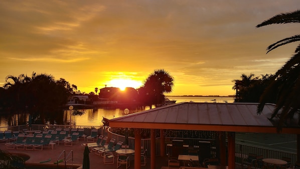 A sunset view from a poolside area with lounge chairs and a covered seating area.