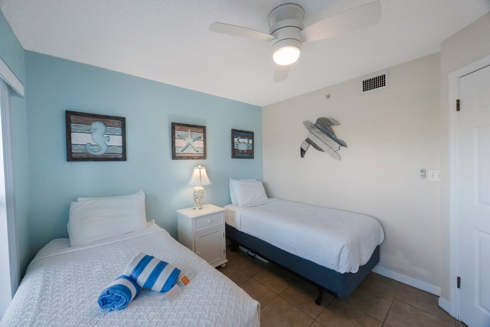 A bedroom with two beds, a nightstand, a ceiling fan, and wall art.
