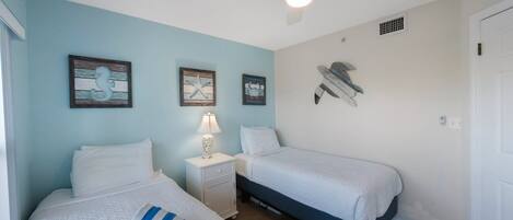 A bedroom with two beds, a nightstand, a ceiling fan, and wall art.