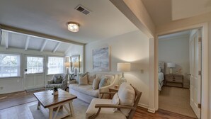A spacious living room with a sofa, armchairs, and a coffee table. There is a painting on the wall and a lamp on a side table.
