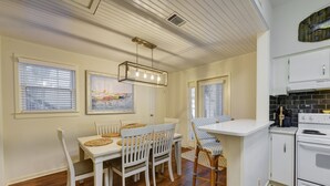 A dining area with a white table and chairs, a hanging light fixture, and a kitchen with white cabinets and a stove.