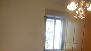 A bedroom with a single bed, a nightstand with a lamp, a window with blinds, and wooden wardrobe doors. - Dependance "L Antica Locanda" (Reggio Calabria)