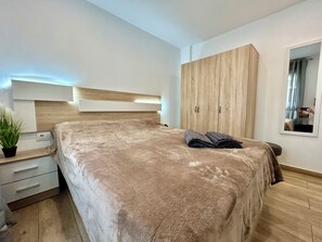 Ein Schlafzimmer mit einem großen Bett, einem Holzschrank, einem Nachttisch mit Pflanze und einem Spiegel an der Wand.