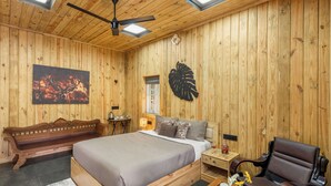 A wooden-paneled room with a bed, bench, chair, and a table with cups and a vase.