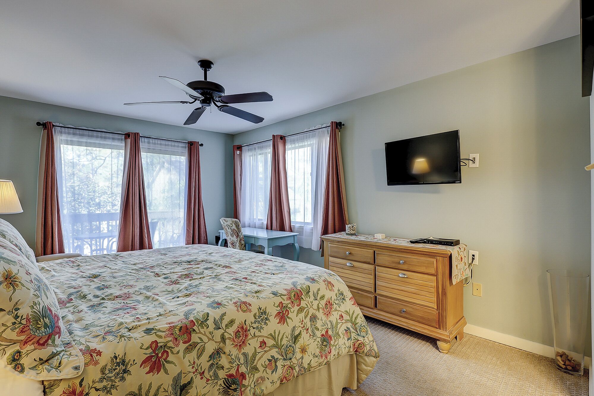 Une chambre à coucher comprenant un lit, une commode, un bureau, une chaise, un ventilateur de plafond et un téléviseur.