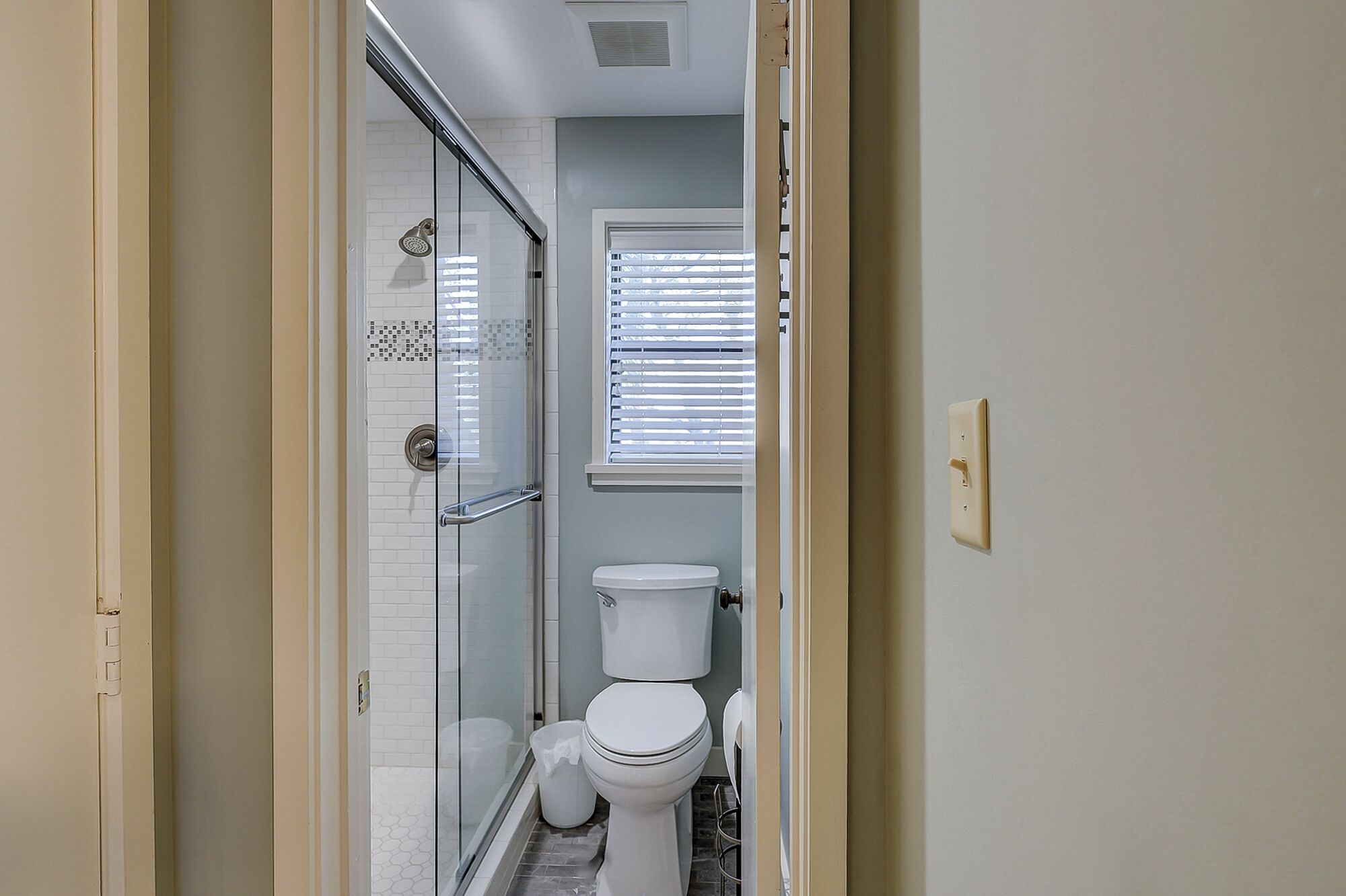 Une petite salle de bain avec une douche en verre, des toilettes et une fenêtre avec des stores.