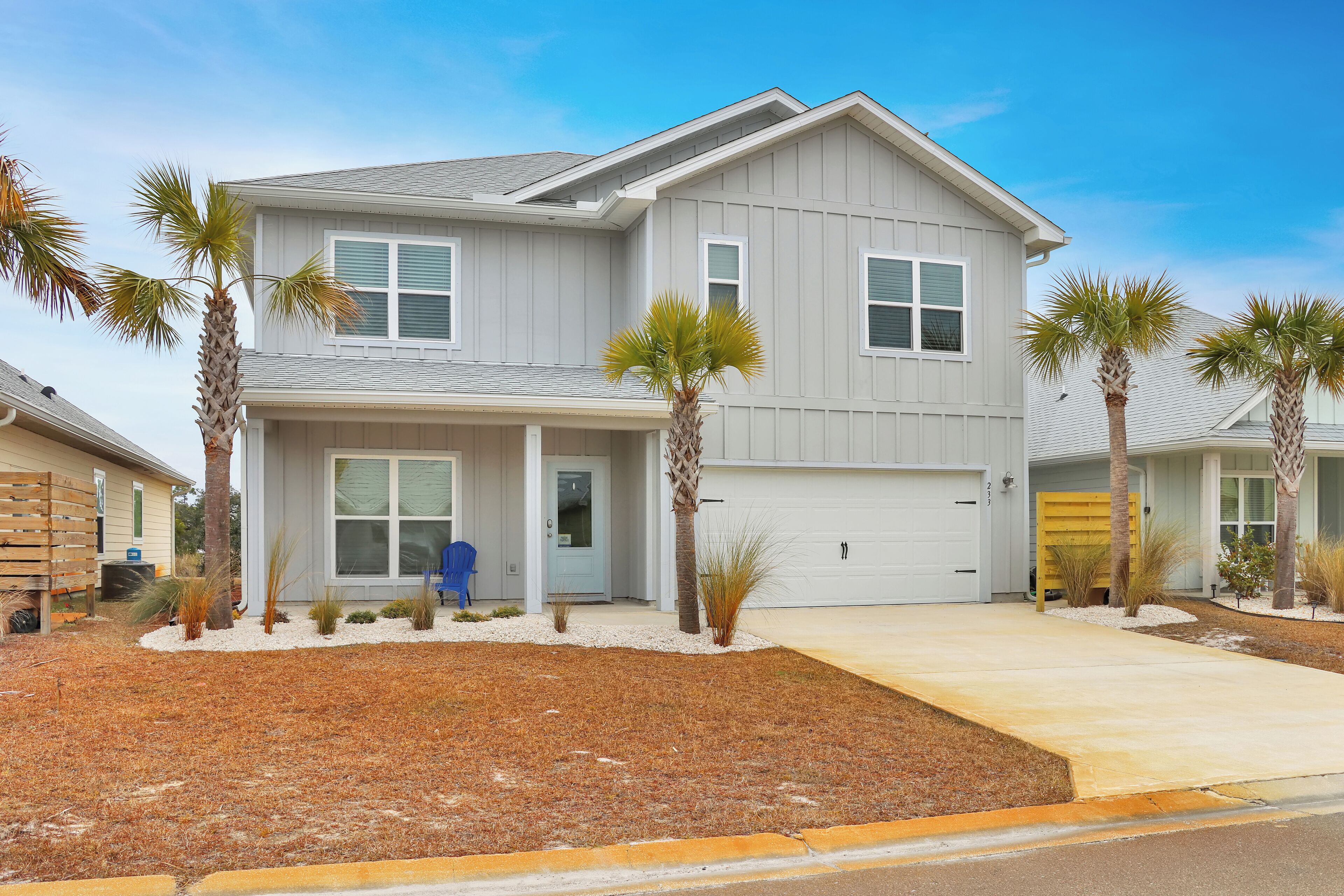 A two-story house with a garage, a covered porch, and palm trees.