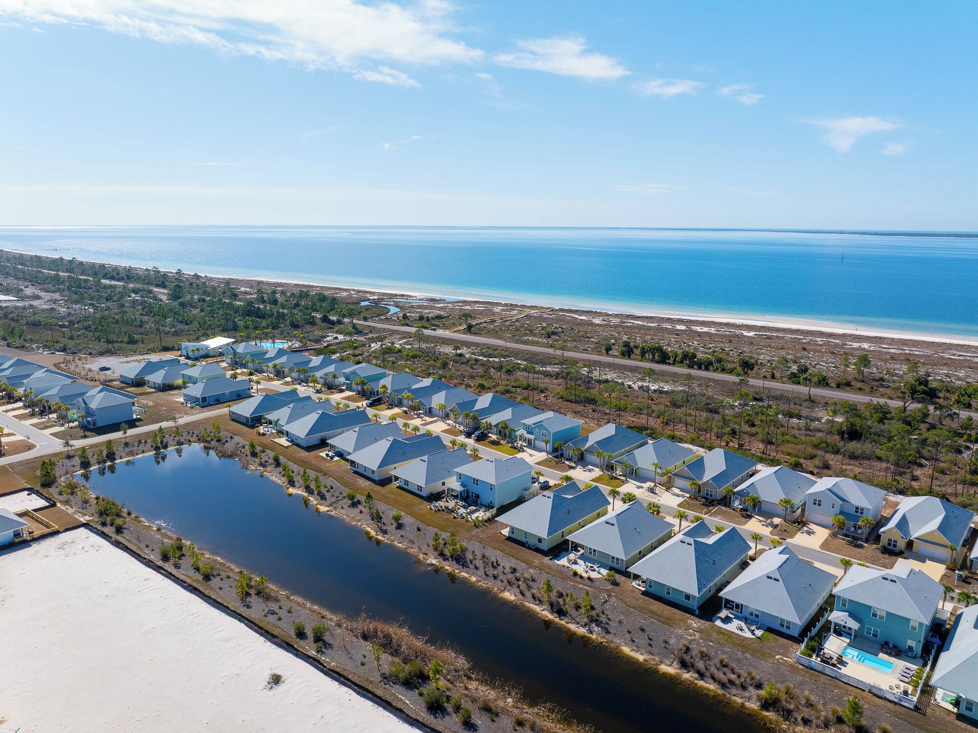 An aerial view of a coastal resort with multiple blue-roofed buildings, a large body of water, and a beach in the background.