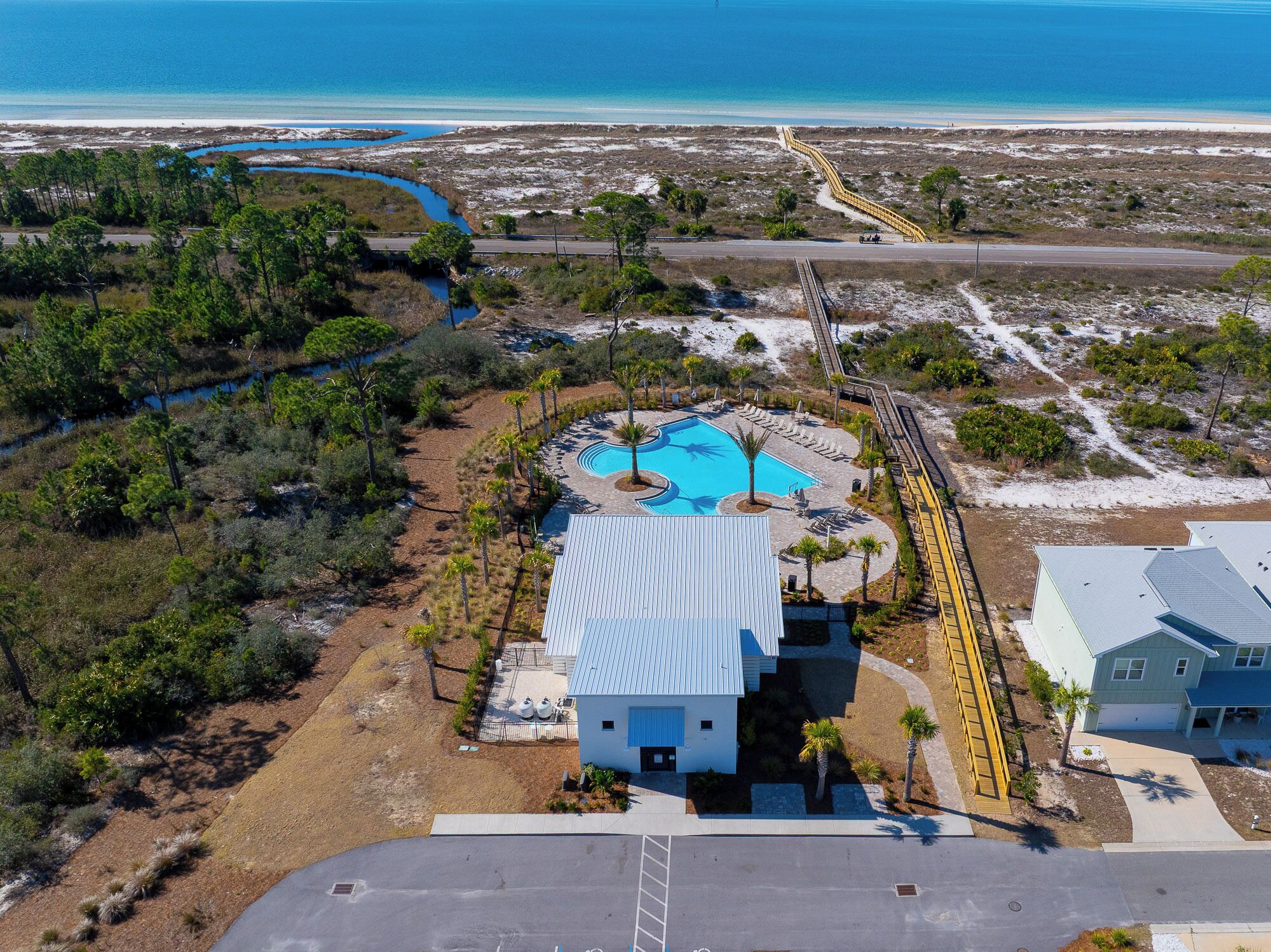 An aerial view of a coastal property with a swimming pool, a small house, and a beach access road.