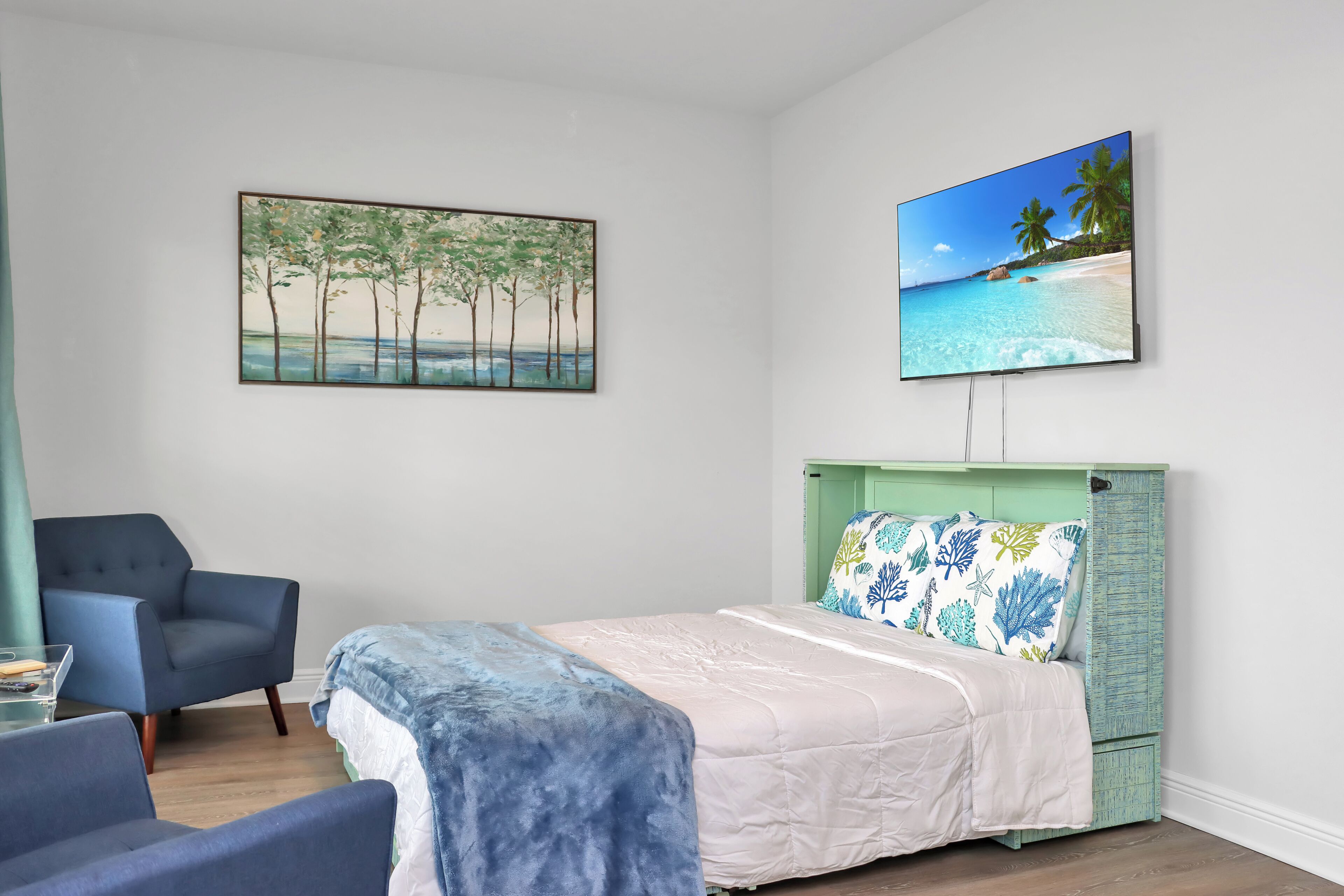 A bedroom with a bed, a chair, a desk, and two paintings on the wall.