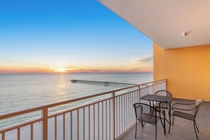Ein Balkon mit Tisch und Stühlen mit Blick auf das Meer bei Sonnenuntergang.