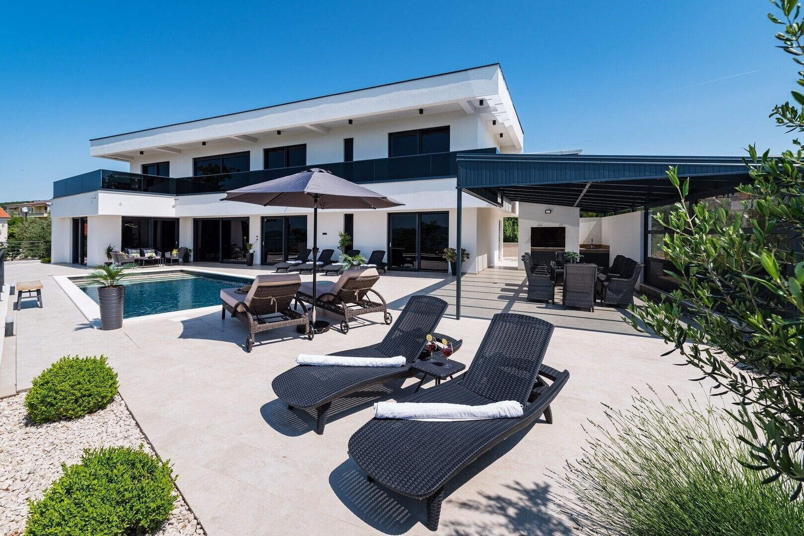 A modern two-story house with a swimming pool, outdoor seating, and a covered patio area.