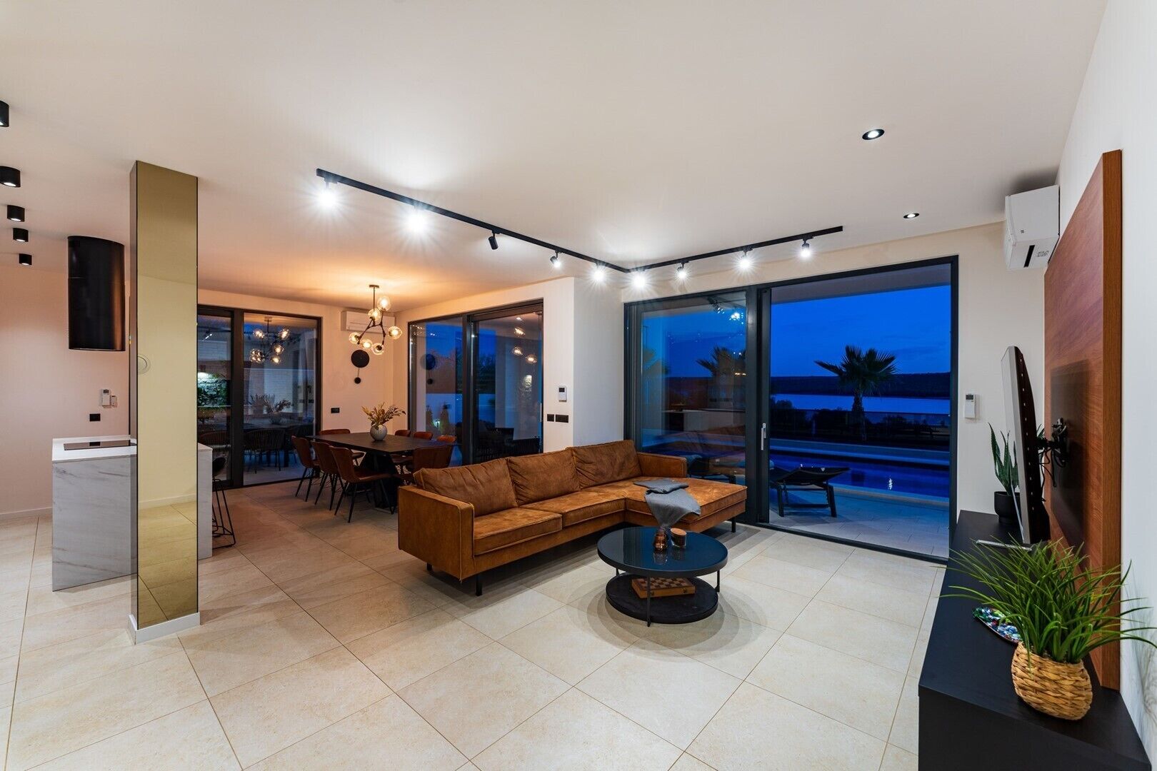 A modern living room with a sectional sofa, a dining area, and a large sliding glass door leading to a pool.