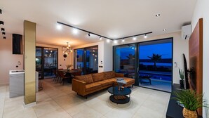 A modern living room with a sectional sofa, a dining area, and a large sliding glass door leading to a pool. - Luxury Villa Spectrum pool 32m2 sauna, family, sea view, bbq (Posedarje)
